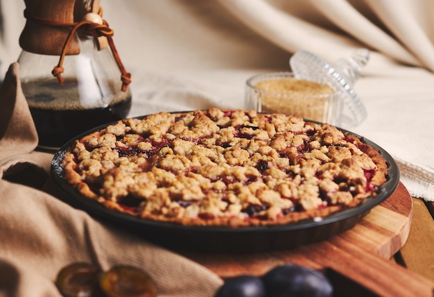 Deliziosa torta di prugne con caffè Chemex e ingredienti con tessuto su un tavolo in legno con tessuto