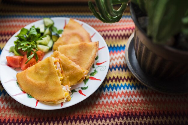 Deliziosa torta vicino insalata di verdure sul piatto vicino a vaso di fiori