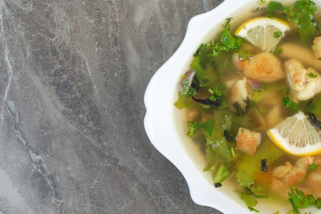 Deliziosa zuppa con verdure e fette di limone sul piatto bianco.