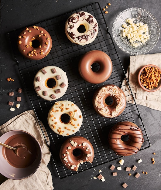 Deliziose ciambelle ricoperte di glassa di cioccolato bianco e marrone con gli ingredienti su un tavolo