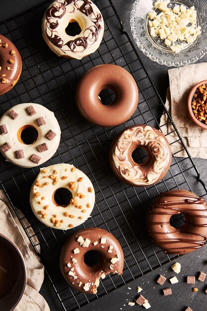 Deliziose ciambelle ricoperte di glassa di cioccolato bianco e marrone con gli ingredienti su un tavolo