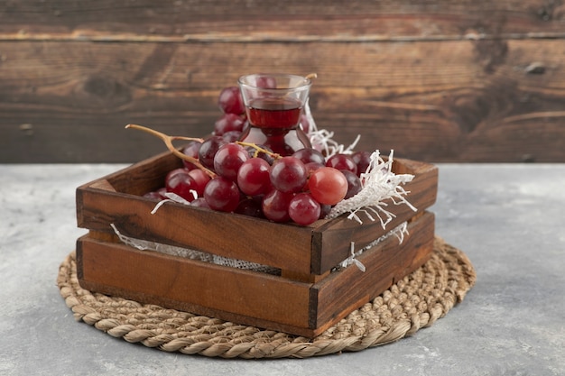 Deliziose uve mature e bicchiere di succo in una scatola di legno.