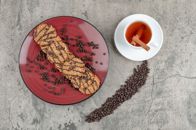 Deliziosi biscotti cosparsi di gocce di cioccolato sulla targhetta rossa e tazza di tè.