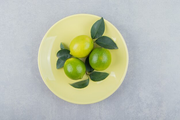 Deliziosi frutti di lime con foglie su piatto giallo