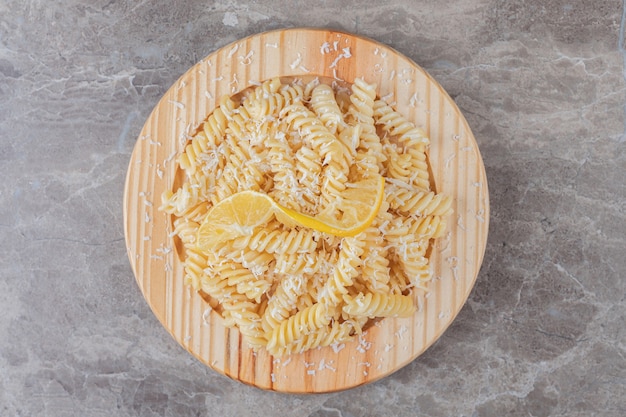 Deliziosi fusilli con fette di limone sul piatto di legno, sul marmo.