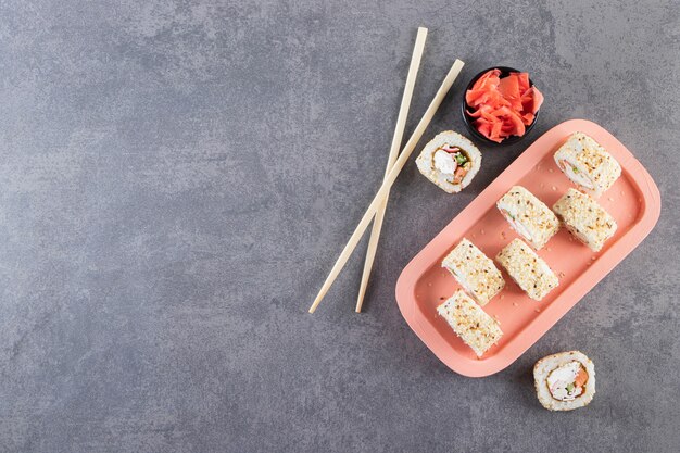 Deliziosi involtini di sushi freschi con salsa di soia e bacchette di legno posizionati su una tavola di legno.