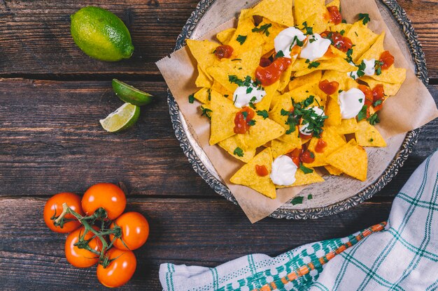 Deliziosi nachos messicani nel piatto; fette di limone; pomodorini e stoffa sul tavolo