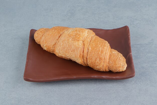 Delizioso croissant sulla piastra, sullo sfondo di marmo. Foto di alta qualità