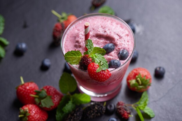 Delizioso frullato di fragole, gelsi e mirtilli guarnito con frutti di bosco freschi e menta in vetro. focalizzazione morbida. bellissimo antipasto lamponi rosa, benessere e concetto di perdita di peso.