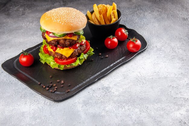 Delizioso panino fatto in casa e patatine fritte ketchup su lavagna nera sul lato destro sulla superficie grigia del ghiaccio ice