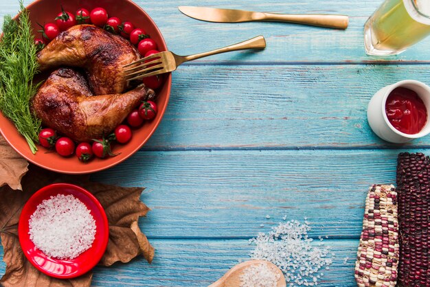 Delizioso pollo arrosto per cena con birra; sale; salsa; mais e pomodorini sul tavolo