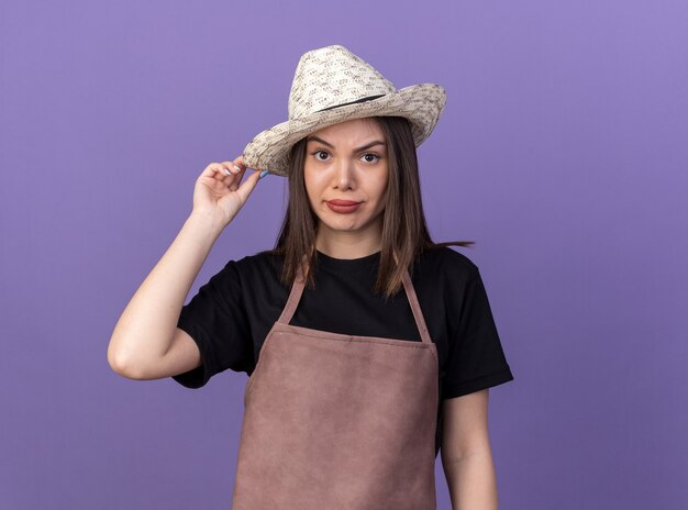 Deluso giardiniere femmina caucasica che indossa e tiene in mano un cappello da giardinaggio