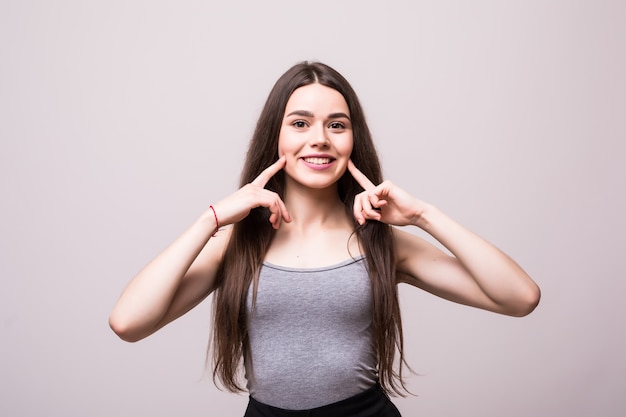 Denti puliti e sani. Giovane bella donna sorridente punta le dita ai denti su un muro grigio.