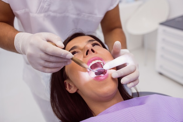 Dentista che esamina i denti pazienti con uno specchio di bocca