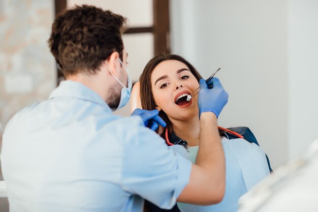 Dentista che fa la pulizia professionale dei denti con il cotone, giovane paziente femminile presso lo studio dentistico.