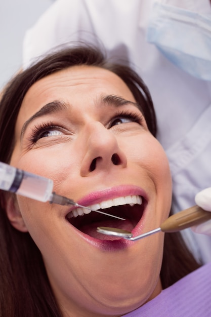 Dentista che inietta anestetici nella bocca paziente femminile spaventata