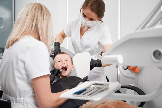 Dentista e assistente che esaminano i denti del bambino nello studio dentistico