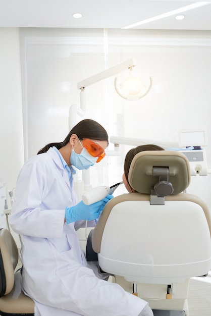 Dentista femminile asiatico che cura il riempimento del dente del paziente con luce ultravioletta