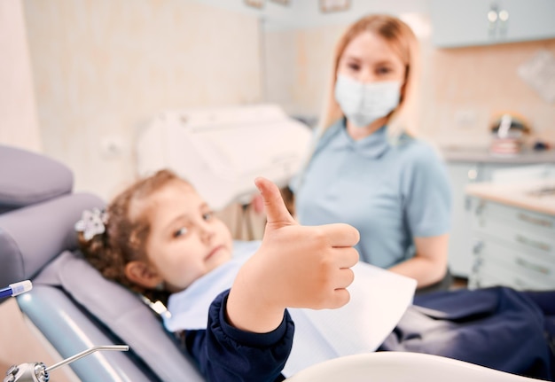 Dentista femminile e bambina sveglia che danno i pollici in su