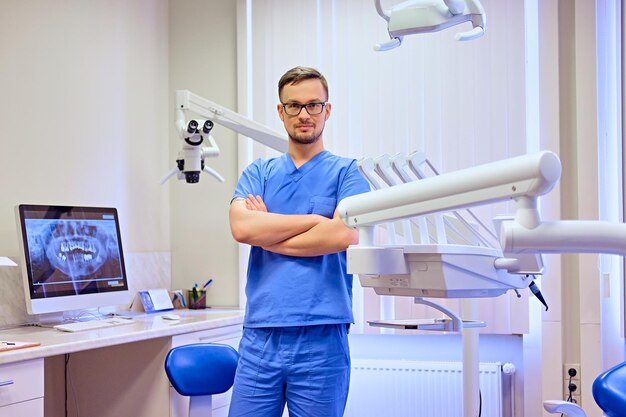 Dentista maschio bello in una stanza con attrezzature mediche sullo sfondo.