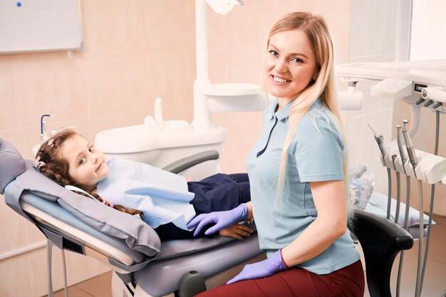 Dentista pediatrico seduto accanto a una bambina adorabile in studio dentistico