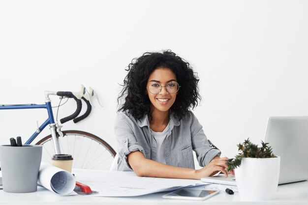 Designer studentessa sorridente seduto al suo posto di lavoro circondato da gadget