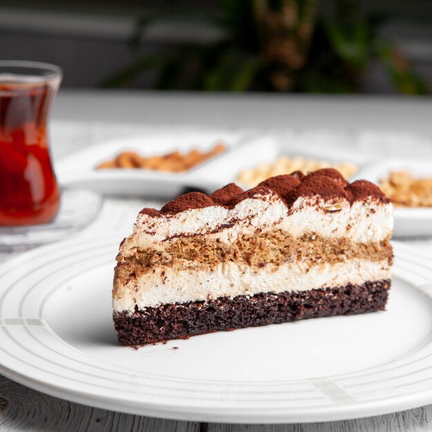 Dessert delizioso del primo piano in piatto con tè, dadi su fondo di legno bianco.