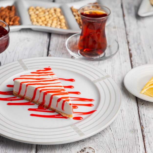 Dessert delizioso di vista dell'angolo alto in piatto con tè, noci, marmellata di frutta, limoni affettati su fondo di legno bianco.