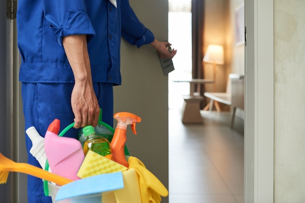 Detergente irriconoscibile che cammina nella camera d'albergo con strumenti e detergenti