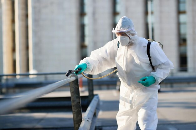 Detergente maschile in tuta protettiva che disinfetta l'area pubblica della città a causa dell'epidemia di coronavirus