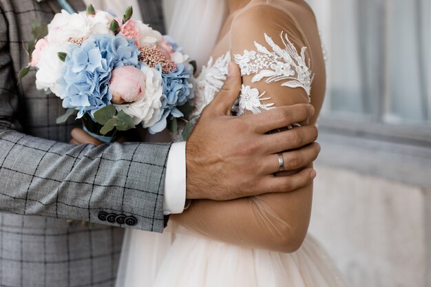 Dettagli del matrimonio, mano di uno sposo con anello nuziale e tenero bouquet da sposa nelle mani della sposa