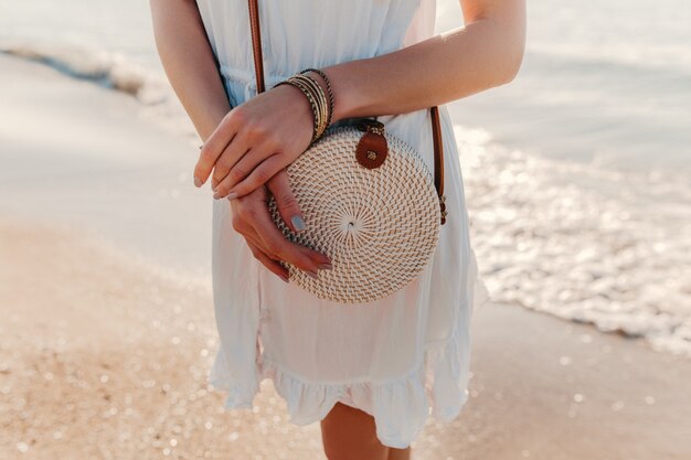 Dettagli di moda del primo piano della donna in abito bianco con stile estivo borsa borsa di paglia su accessori da spiaggia