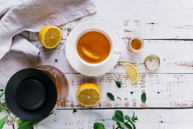 Dettaglio della tazza di tè con il limone e la menta fresca sulla tavola di legno bianca
