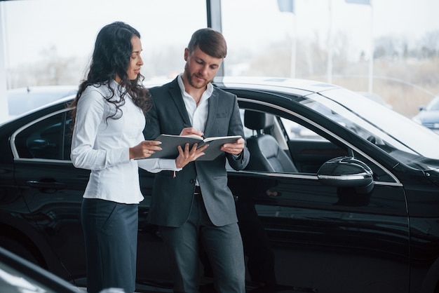 Devi accedere a quel documento. Cliente femminile e uomo d'affari barbuto elegante moderno nel salone dell'automobile