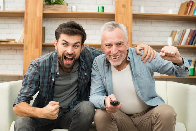 Di età compresa tra uomo felice con telecomando e giovane ragazzo piangere guardando la TV sul divano