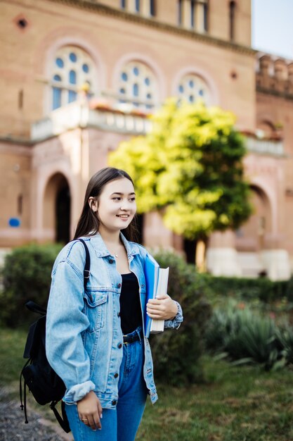 Di nuovo alla ragazza dello studente della scuola che guarda al lato in libri della tenuta del parco e taccuini che indossano zaino.