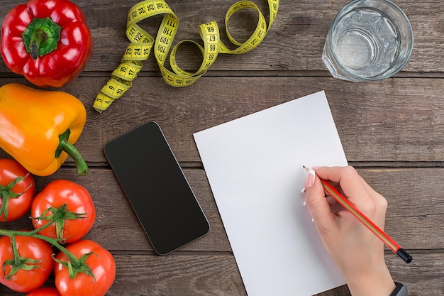 Dieta concettuale, piano dimagrante con vista dall'alto di verdure mock up. Una mano femminile in un braccialetto sportivo scrive un articolo sulla corretta alimentazione