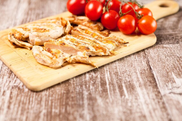 Dieta sana. Petto di pollo fresco alla griglia su tavola di legno accanto ai pomodori. Cena e stile di vita sani