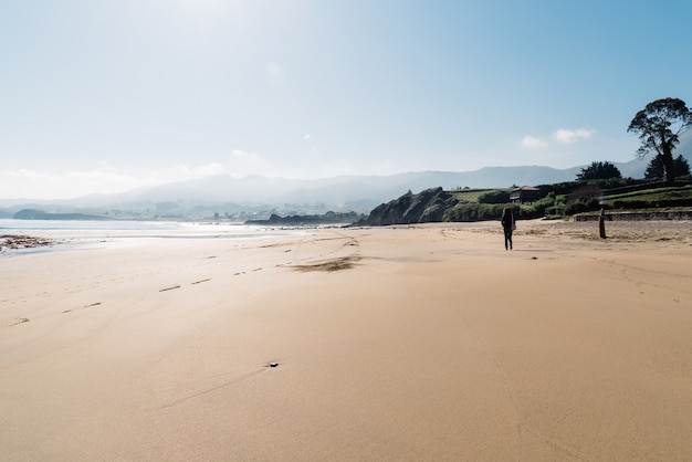 Dietro il colpo di una donna che cammina sulla spiaggia di sabbia vicino alla riva con le montagne