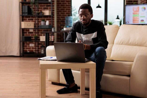 Dipendente afroamericano che lavora su laptop per pianificare presentazioni aziendali e nuove app per lo sviluppo di software nella sicurezza informatica. Impiegato che utilizza il rapporto aziendale per inviare e-mail