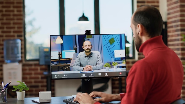Dipendente dell'azienda che utilizza la videoconferenza online per avere una conversazione remota in ufficio. Lavoratore maschio che parla con un consulente in videoconferenza, partecipando a una riunione informativa sul computer.