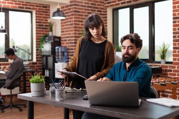 Direttori esecutivi che analizzano documenti con statistiche di marketing che discutono della strategia aziendale mentre lavorano alla collaborazione aziendale nell'ufficio di avvio del muro di mattoni. Gli uomini d'affari fanno brainstorming di idee