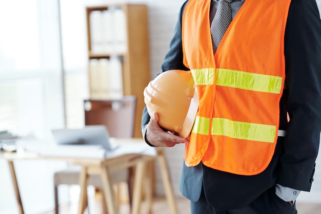 Dirigente maschio irriconoscibile del settore delle costruzioni che posa in giubbotto di sicurezza, con l'elmetto protettivo