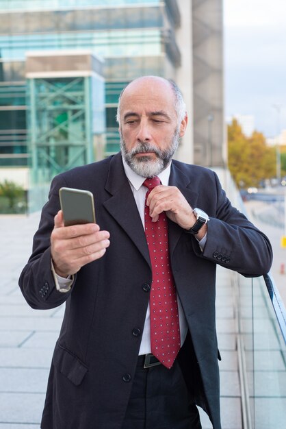 Dirigente maturo serio con il messaggio di lettura dello smartphone