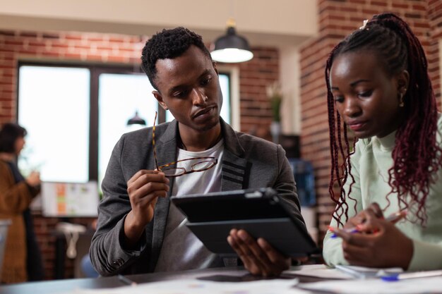 Dirigenti esecutivi che analizzano le statistiche di marketing sul computer tablet idee di brainstorming per il progetto aziendale durante la riunione di lavoro nell'ufficio di avvio. Strategia di pianificazione degli imprenditori multietnici