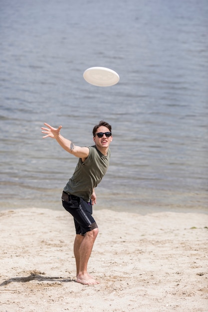 Disco di frisbee di lancio dell&#39;uomo adulto sulla spiaggia