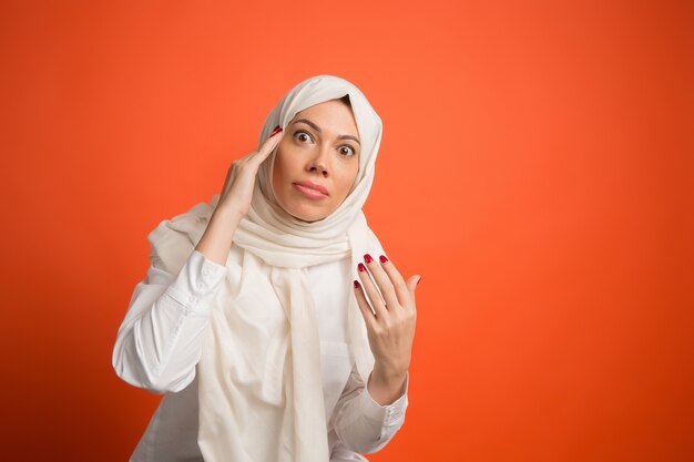 Discuti, sostenendo concept.arab donna in hijab. Ritratto di ragazza, in posa a. sfondo rosso studio. Giovane donna emotiva. Le emozioni umane, il concetto di espressione facciale. Vista frontale.