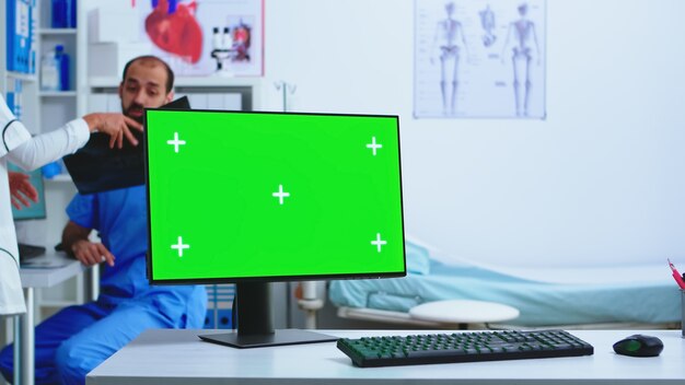 Display del computer con copia spazio disponibile nell'armadietto dell'ospedale e nel medico che tiene i raggi x. Desktop con schermo verde sostituibile in clinica medica mentre il medico sta controllando la radiografia del paziente per la diagnosi