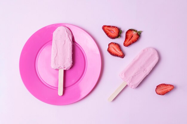 Disposizione del gelato rosa su bastoncini e fettine di fragole