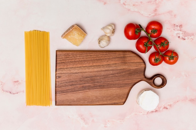 Disposizione della pasta grezza e ingrediente gustoso e tagliere in legno sulla superficie del marmo